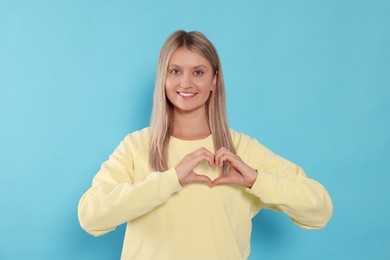 Happy volunteer making heart with her hands on light blue background