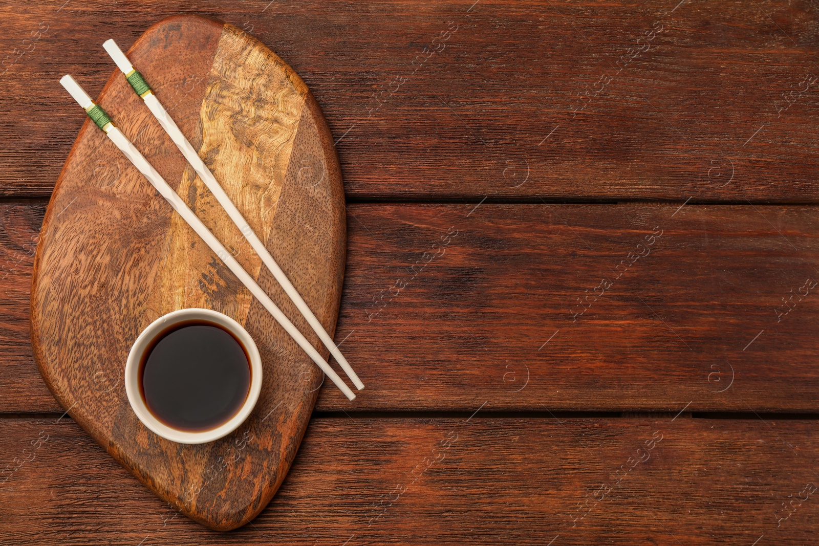 Photo of Bowl with soy sauce and chopsticks on wooden table, top view. Space for text