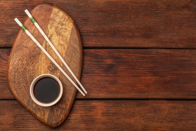 Photo of Bowl with soy sauce and chopsticks on wooden table, top view. Space for text