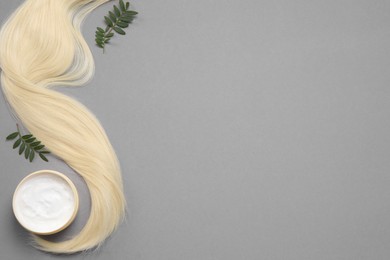 Photo of Lock of healthy blond hair, green twigs and cosmetic product on grey background, flat lay. Space for text