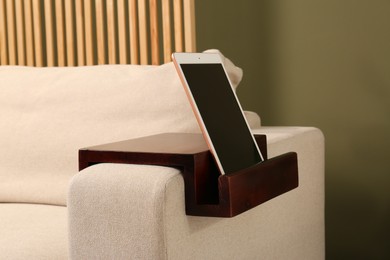 Photo of Tablet on sofa armrest wooden table in room. Interior element