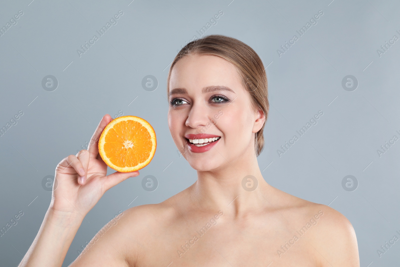 Photo of Young woman with cut orange on grey background. Vitamin rich food