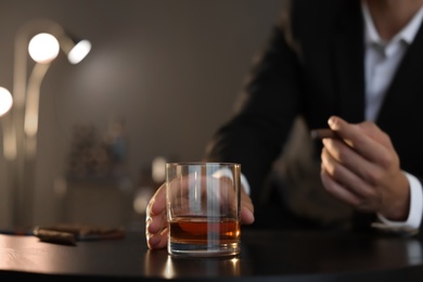 Photo of Man with glass of whiskey and cigar sitting at table, closeup. Space for text