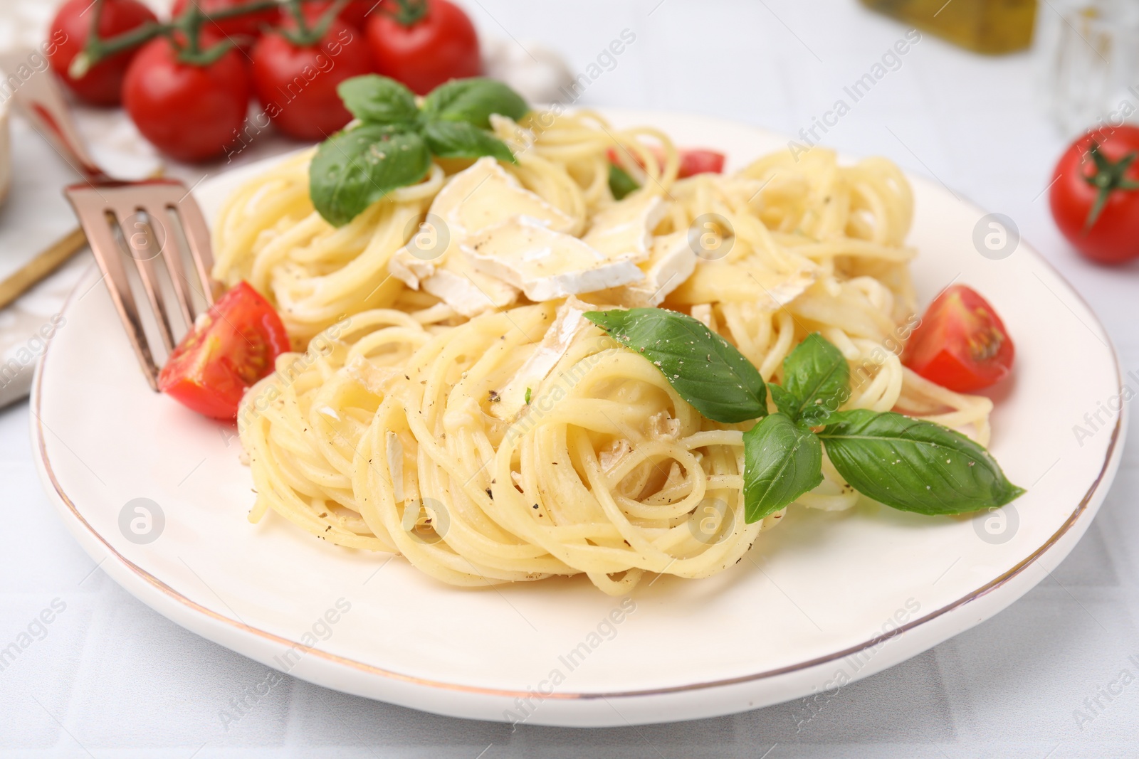 Photo of Delicious pasta with brie cheese, tomatoes and basil leaves on white tiled table, closeup