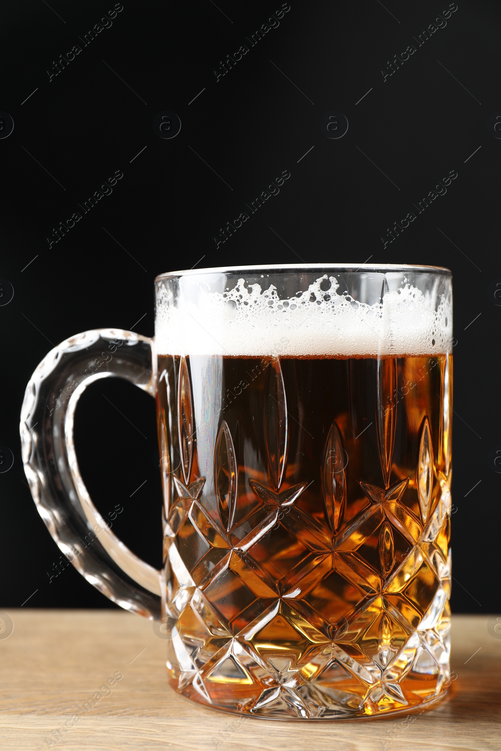 Photo of Mug with fresh beer on wooden table against black background, closeup