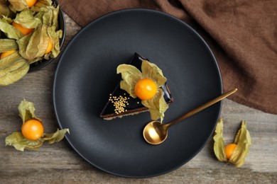 Photo of Piece of tasty cake decorated with physalis fruit on wooden table, flat lay