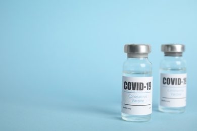 Photo of Vials with coronavirus vaccine on light blue background, space for text