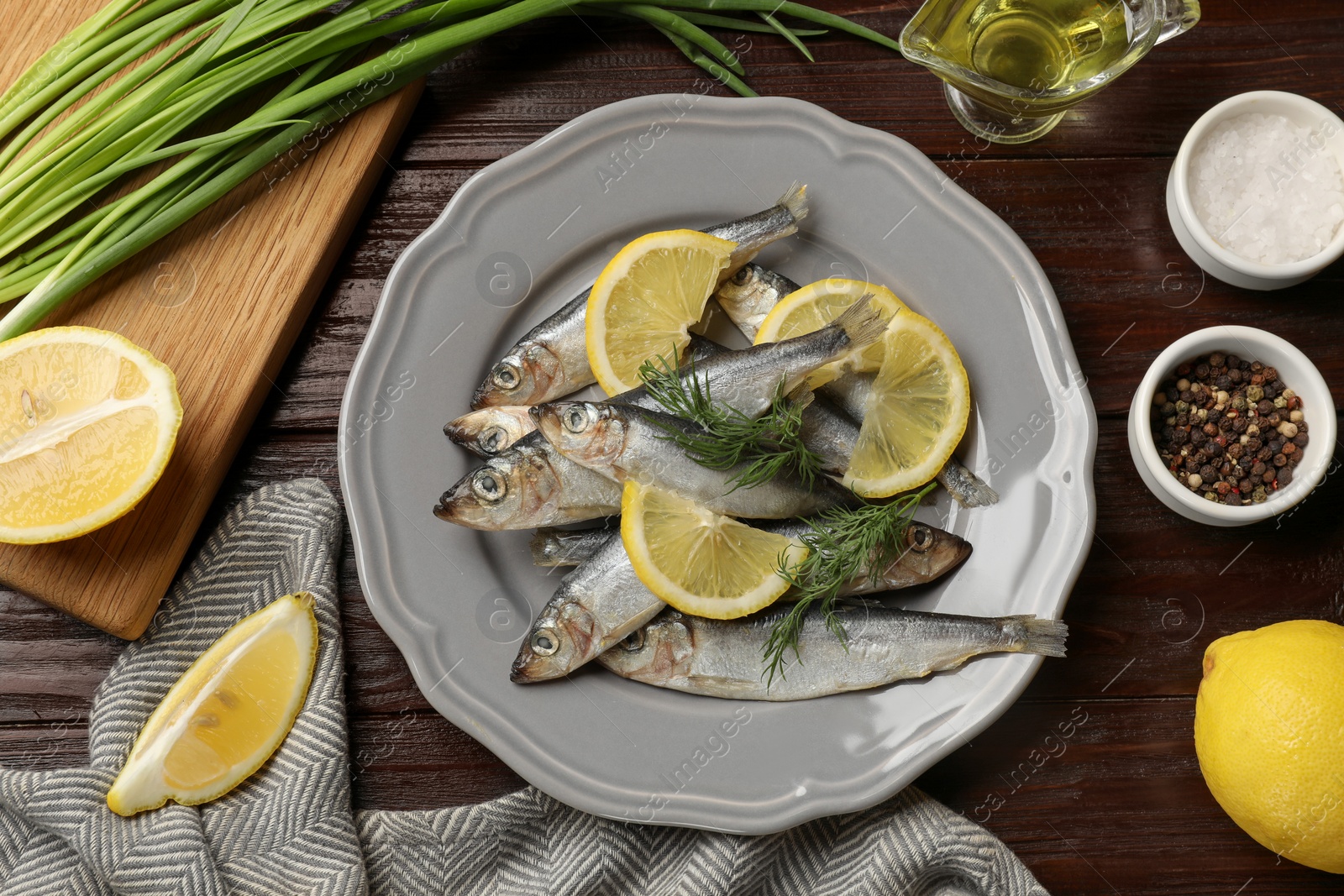 Photo of Fresh raw sprats, green onion, cut lemon and spices on wooden table, flat lay