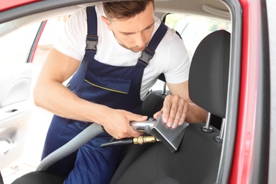 Male worker removing dirt from car seat with professional vacuum cleaner