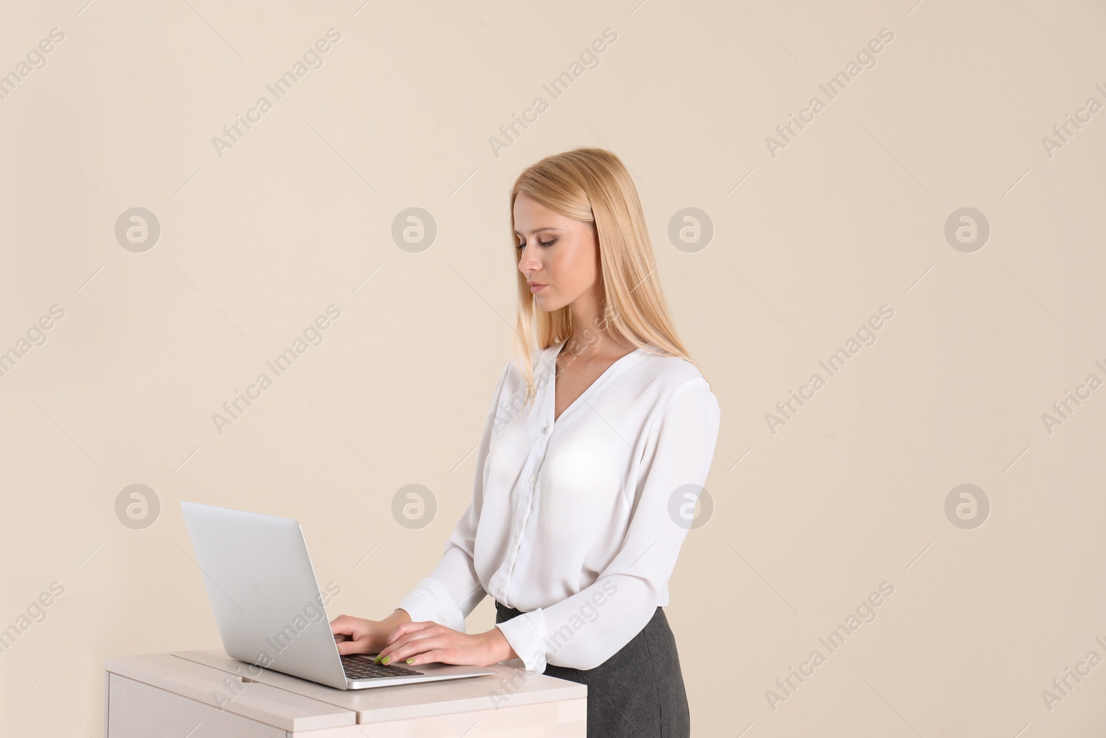 Photo of Young woman using laptop at stand up workplace against light wall