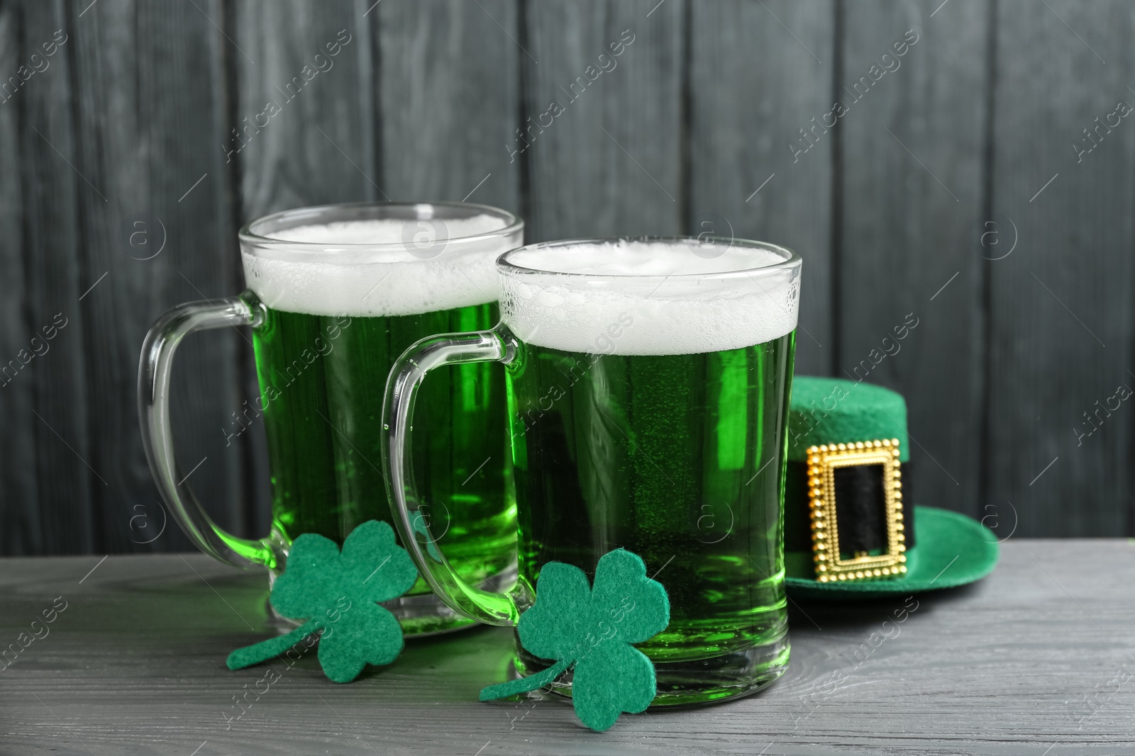 Photo of Green beer, hat and clover leaves on grey wooden table. St. Patrick's Day celebration