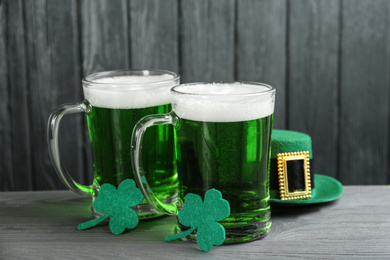 Photo of Green beer, hat and clover leaves on grey wooden table. St. Patrick's Day celebration