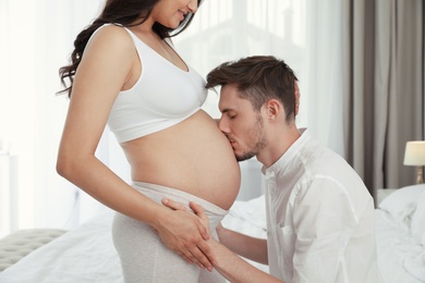 Photo of Young husband kissing his pregnant wife's tummy in bedroom