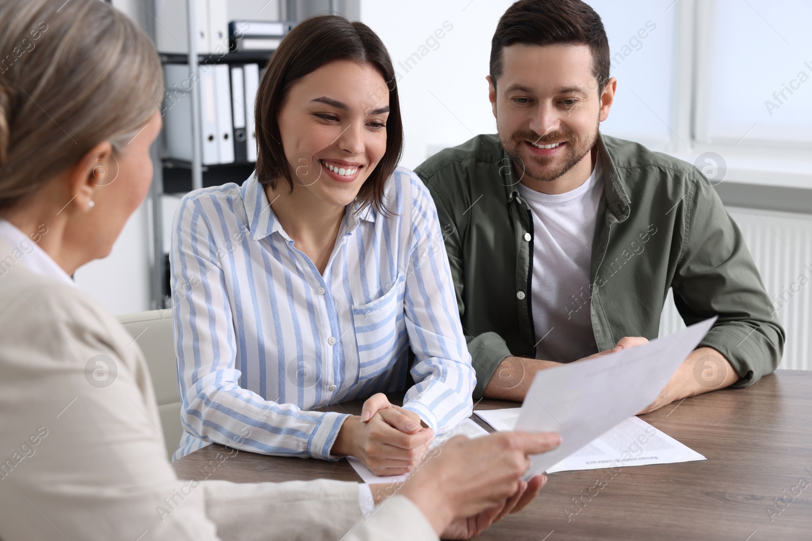 Photo of Young couple consulting insurance agent about pension plan at wooden table indoors