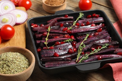 Photo of Raw cut black carrot with pomegranate seeds and thyme in baking dish on table, closeup