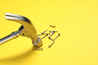 Photo of Hammer and metal nails on yellow background, closeup. Space for text