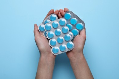 Photo of Woman holding blisters with cough drops on light blue background, top view