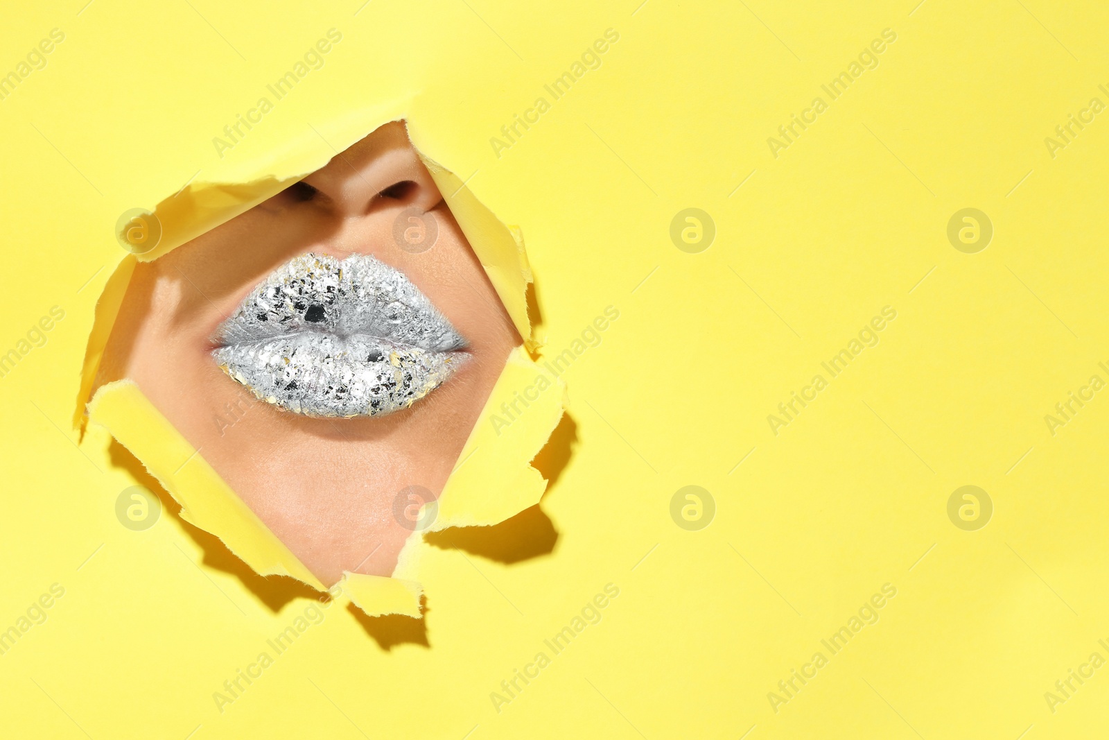 Photo of View of beautiful young woman with creative lips makeup through hole in color paper