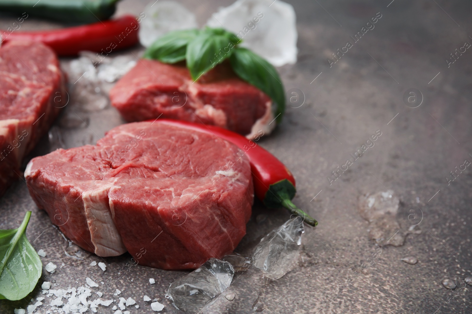 Photo of Fresh raw cut beef, ice cubes and spices on brown table, closeup. Space for text