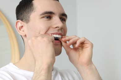 Photo of Young man applying whitening strip on his teeth indoors