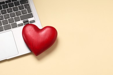 Photo of Long-distance relationship concept. Laptop and decorative heart on beige background, top view with space for text