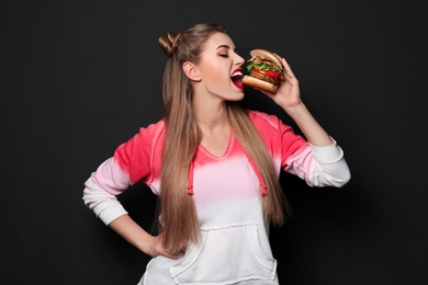 Photo of Pretty woman eating tasty burger on black background