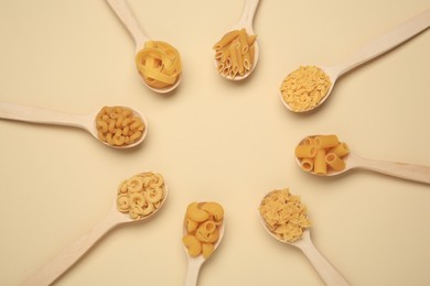 Frame made of spoons with different types of pasta on beige background, flat lay. Space for text