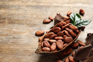 Photo of Pod with cocoa beans and chocolate pieces on wooden table, space for text