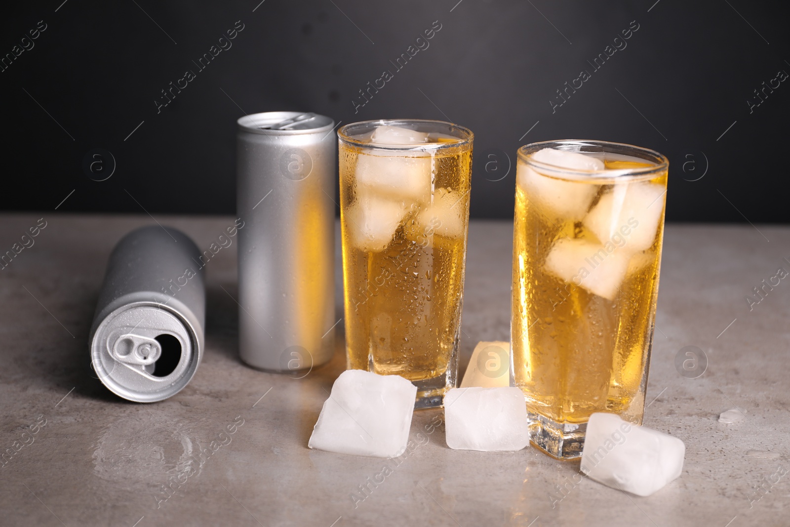 Photo of Tasty energy drink with ice cubes in glasses and aluminium cans on grey table