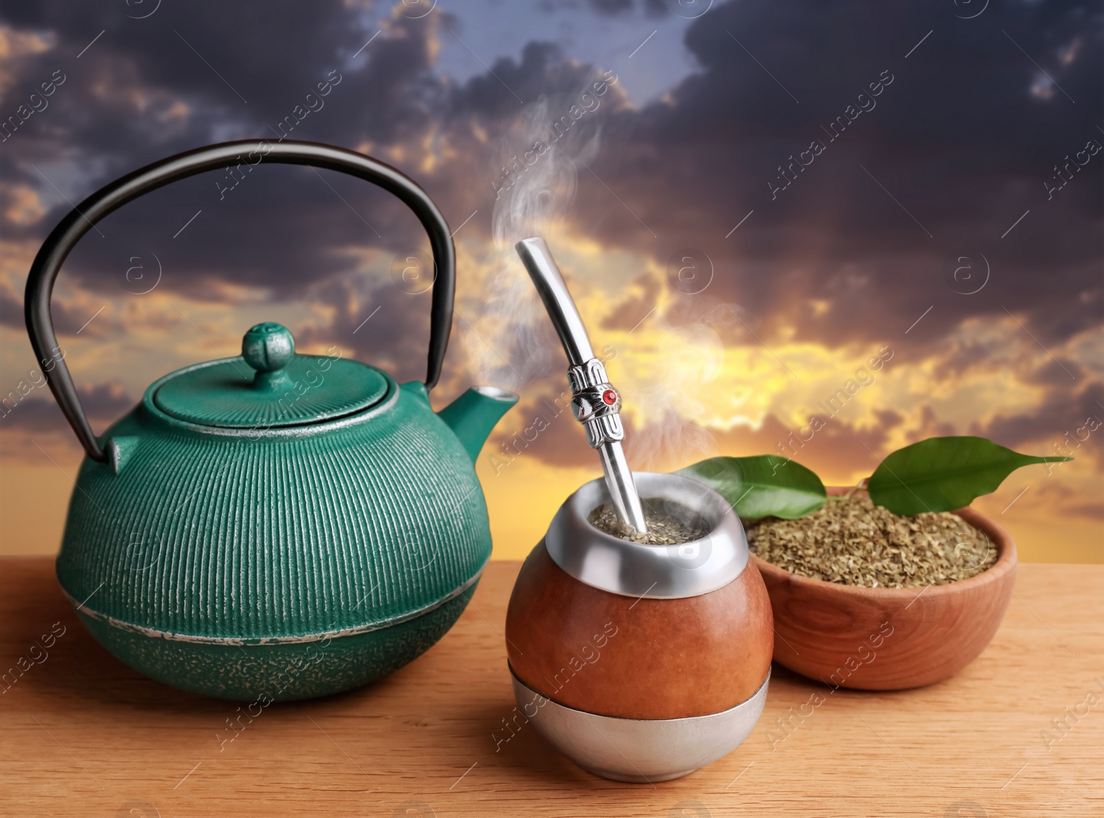 Image of Calabash with mate tea, bombilla and teapot on wooden table outdoors at sunset