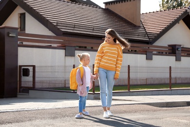 Young mother taking her little child to school on street