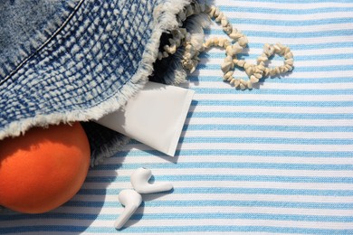 Photo of Denim hat, earphones, orange and beach accessories on striped towel, flat lay. Space for text