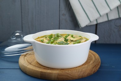 Saucepan of delicious vegetable soup with chicken on blue wooden table