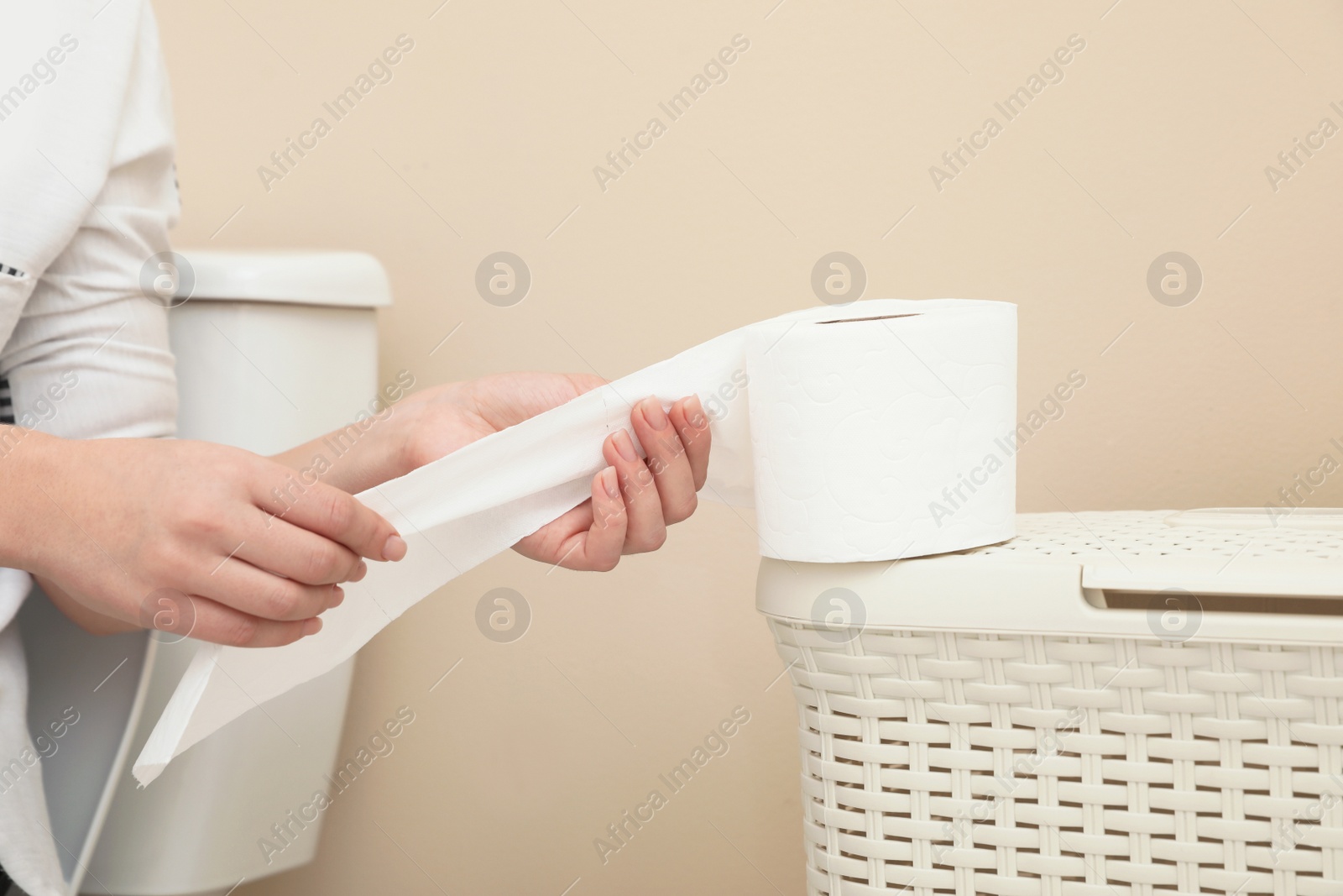 Photo of Woman taking toilet paper from roll in bathroom, closeup