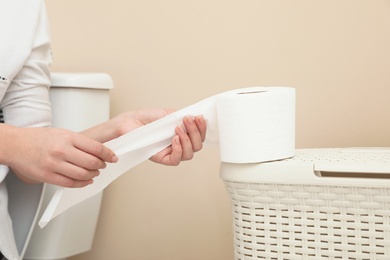 Woman taking toilet paper from roll in bathroom, closeup