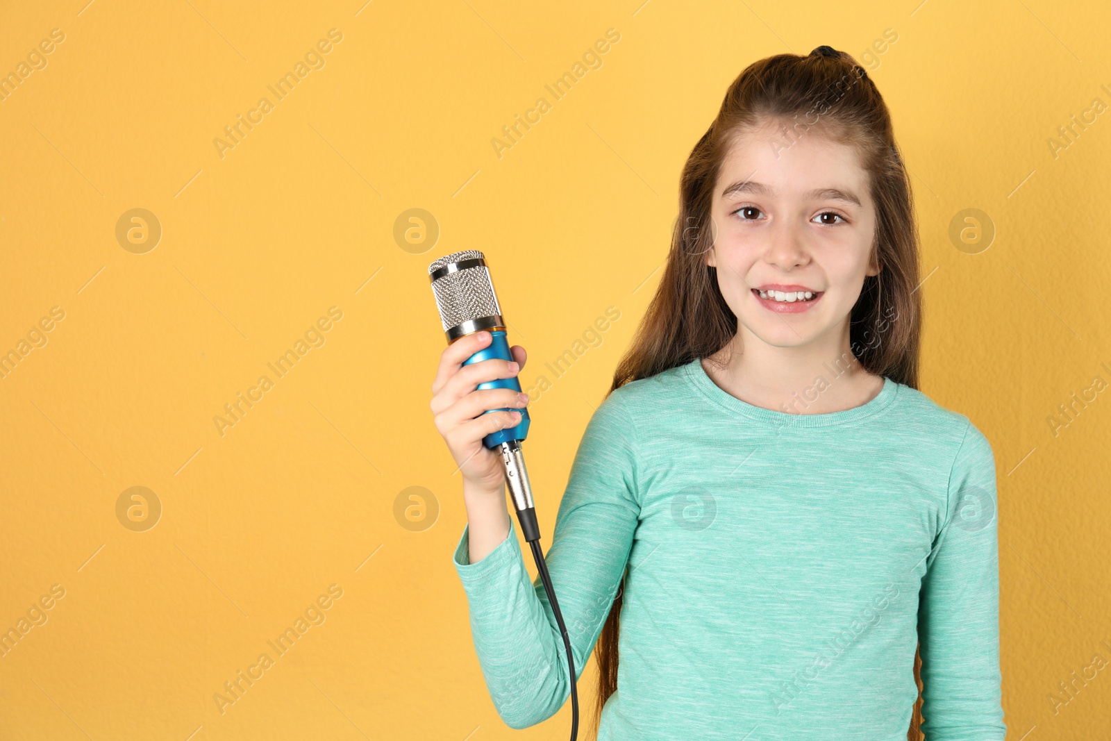 Photo of Cute girl with microphone on color background. Space for text