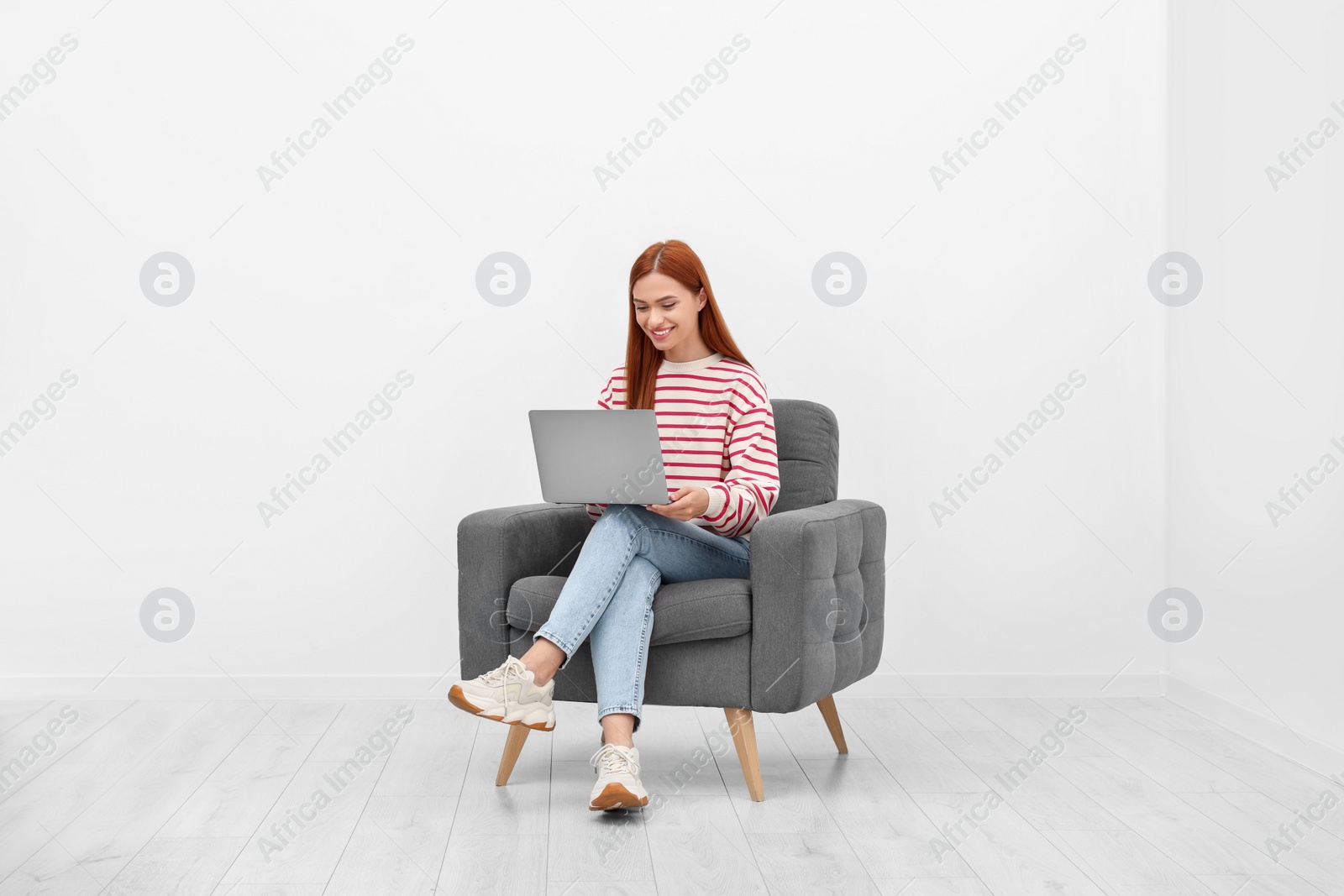 Photo of Happy young woman with laptop sitting in armchair near white wall indoors