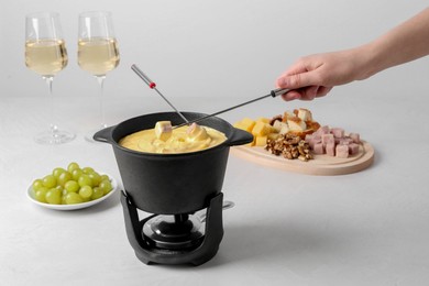 Photo of Woman dipping ham into fondue pot with tasty melted cheese at white table, closeup