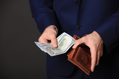 Photo of Businessman with wallet and dollar bills on black background, closeup