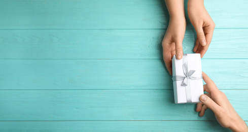 Image of People with gift box and space for text on light blue wooden background, top view. Banner design