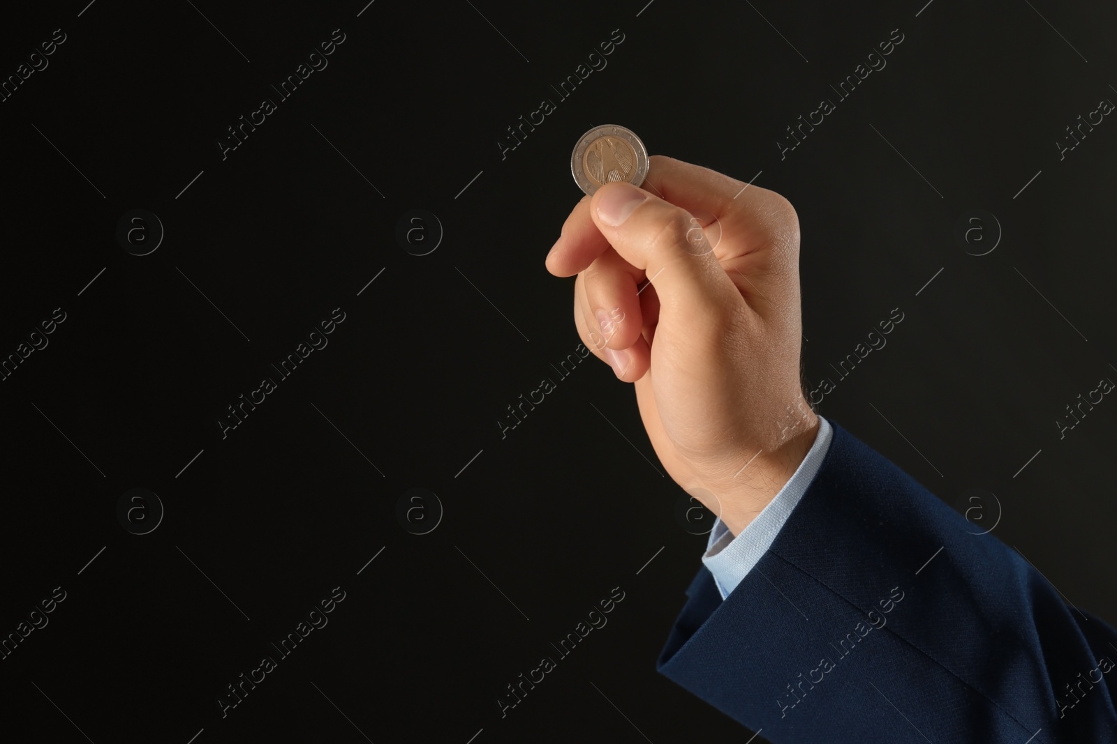 Photo of Young man holding coin on black background, closeup. Space for text