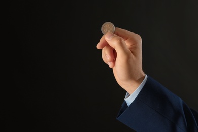 Young man holding coin on black background, closeup. Space for text