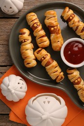 Photo of Cute sausage mummies served with ketchup on wooden table, flat lay. Halloween party food