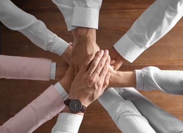 Photo of People holding hands together over wooden background, top view. Unity concept