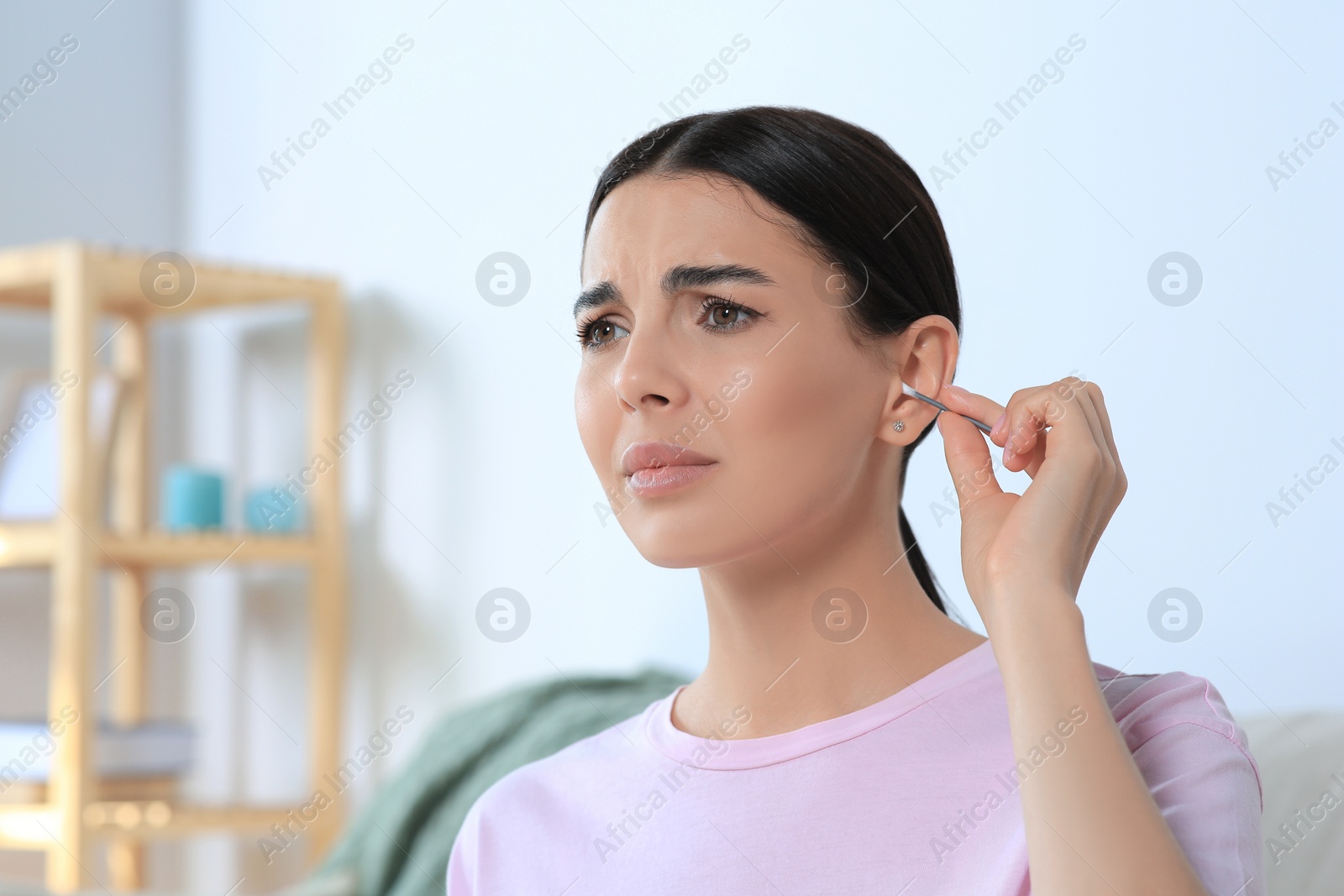 Photo of Young woman cleaning ear with cotton swab at home