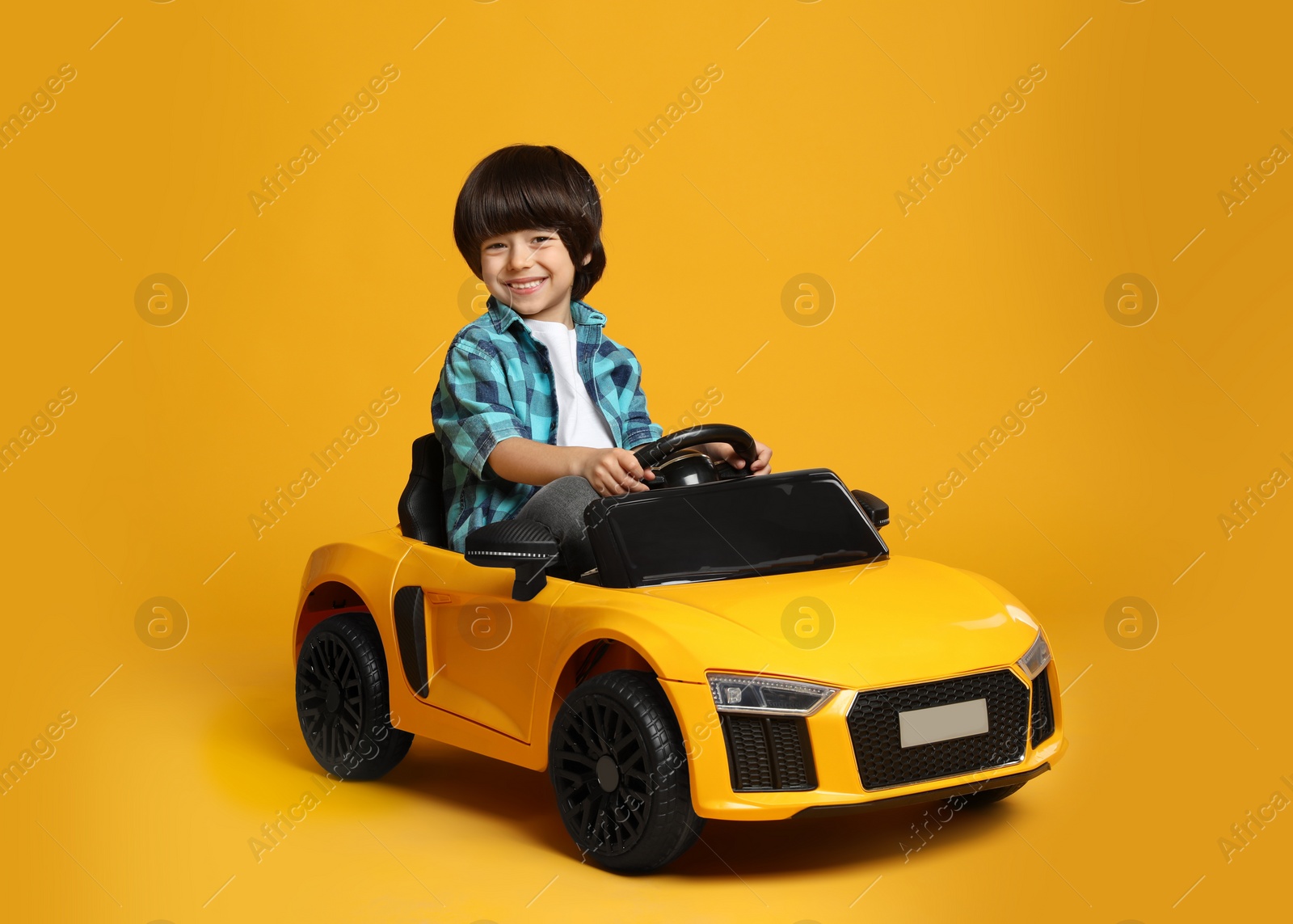 Photo of Cute little boy driving children's electric toy car on yellow background