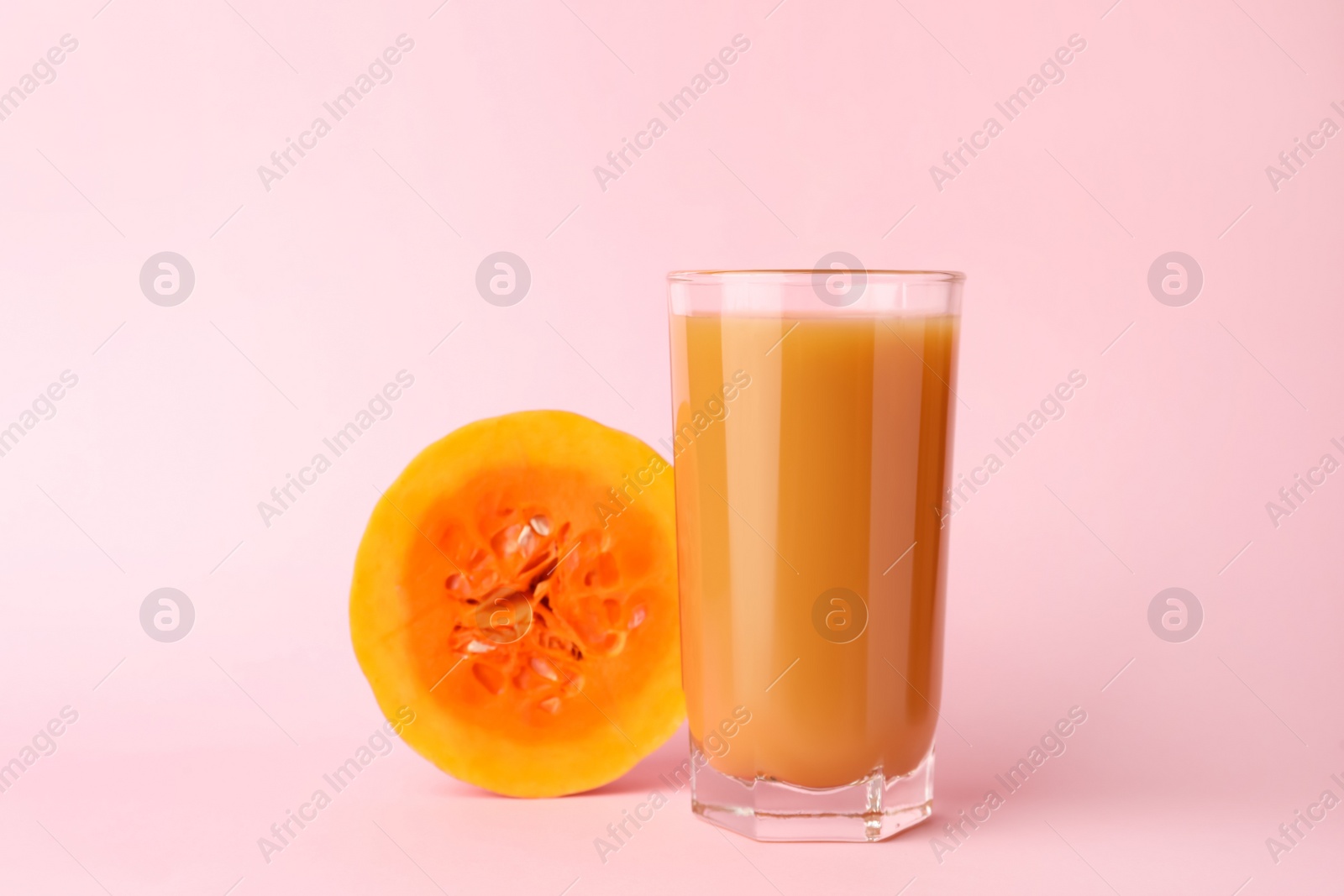 Photo of Tasty pumpkin juice in glass and cut pumpkin on pink background