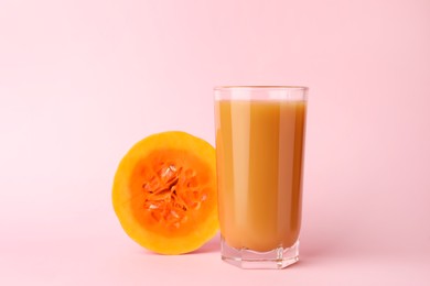 Tasty pumpkin juice in glass and cut pumpkin on pink background