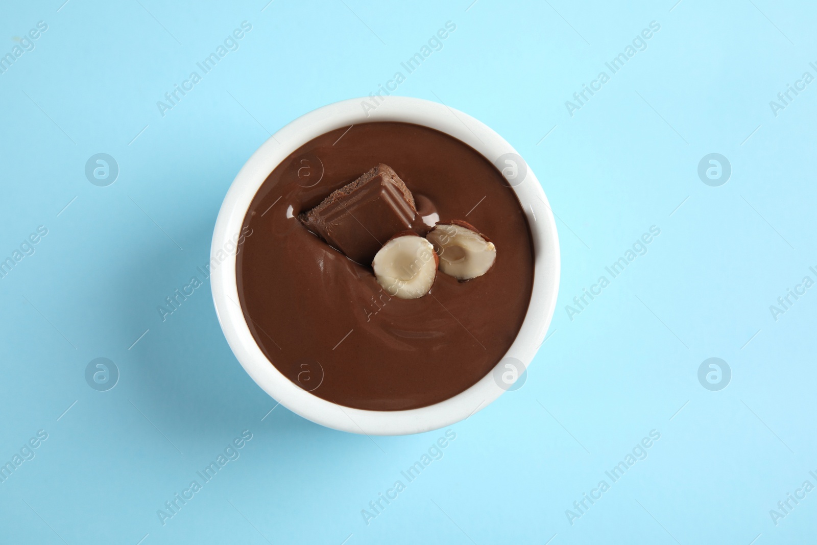 Photo of Ceramic bowl with sweet chocolate cream and hazelnuts on color background, top view