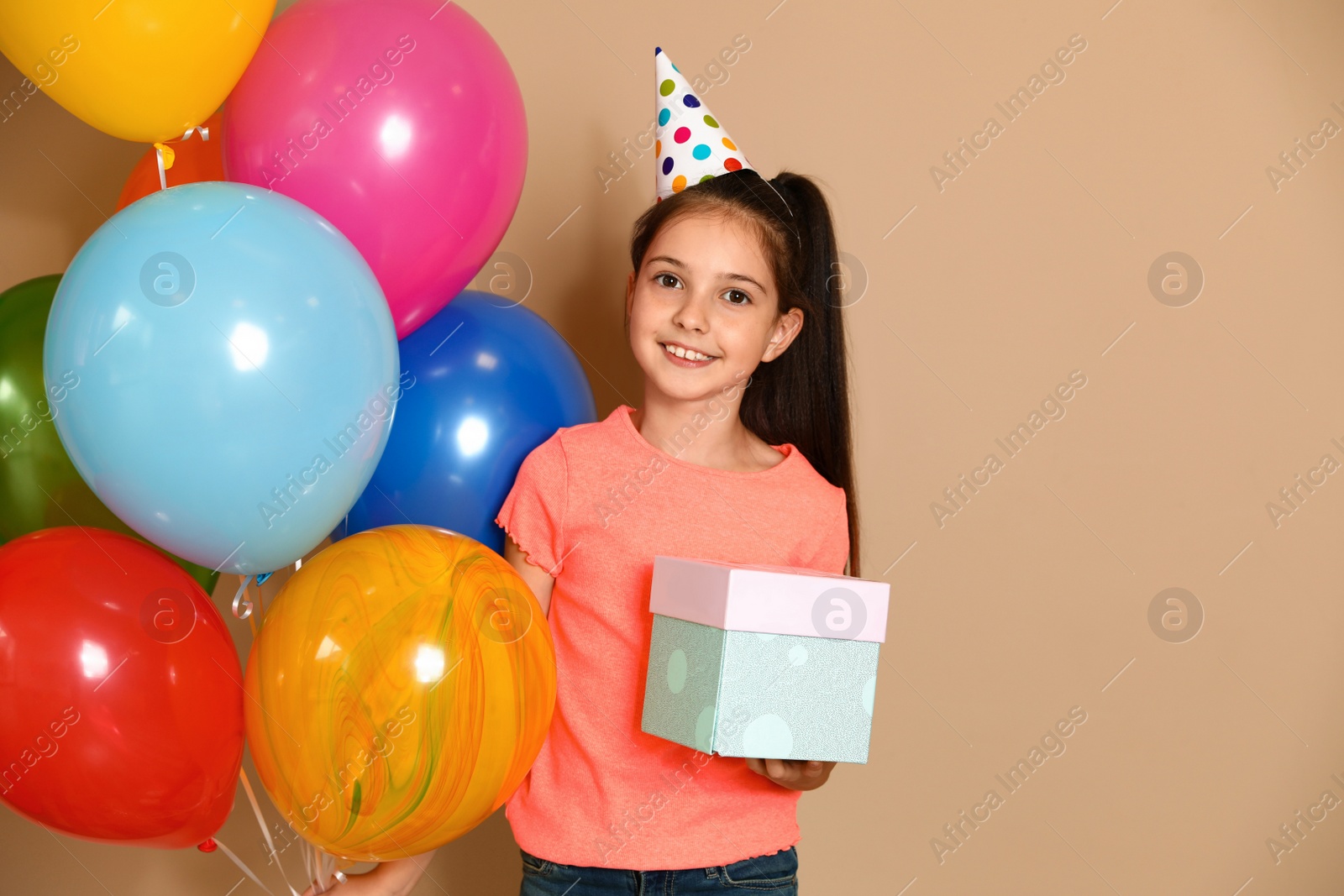 Photo of Happy girl with birthday gift and balloons on brown background